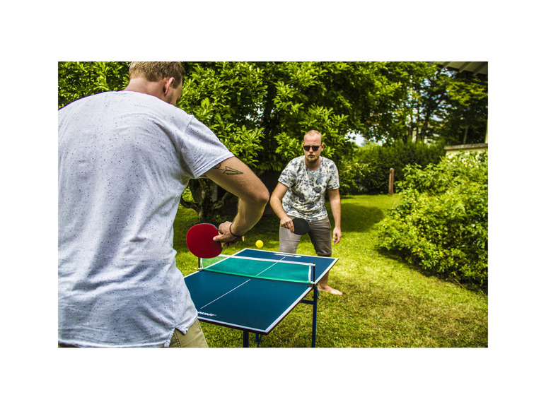 Twee mannen spelen tafeltennis buiten in de tuin.