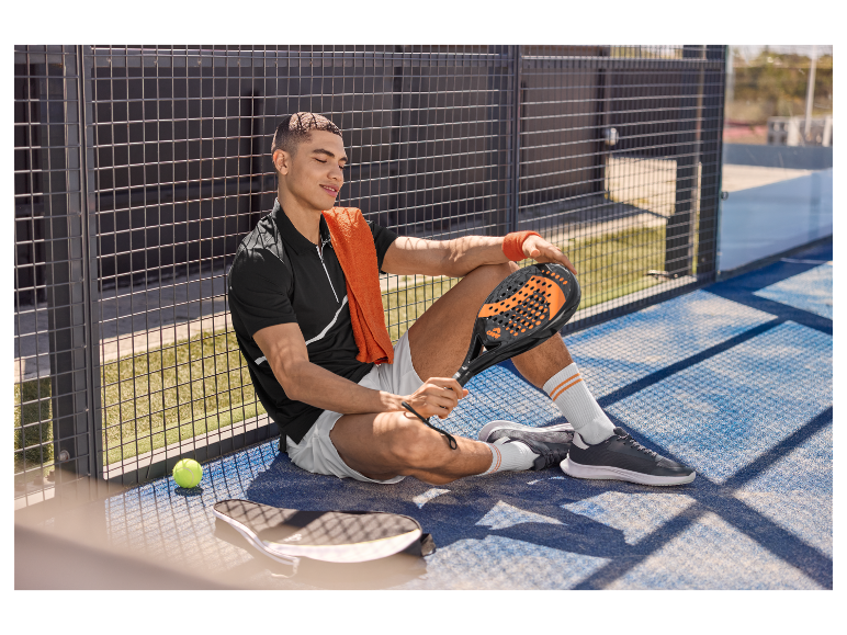 Un joueur de paddle-tennis détendu, tenant sa raquette et assis près d'un terrain.