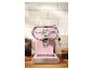 Roze espressomachine met kopjes en koffiebonen op een houten aanrecht.