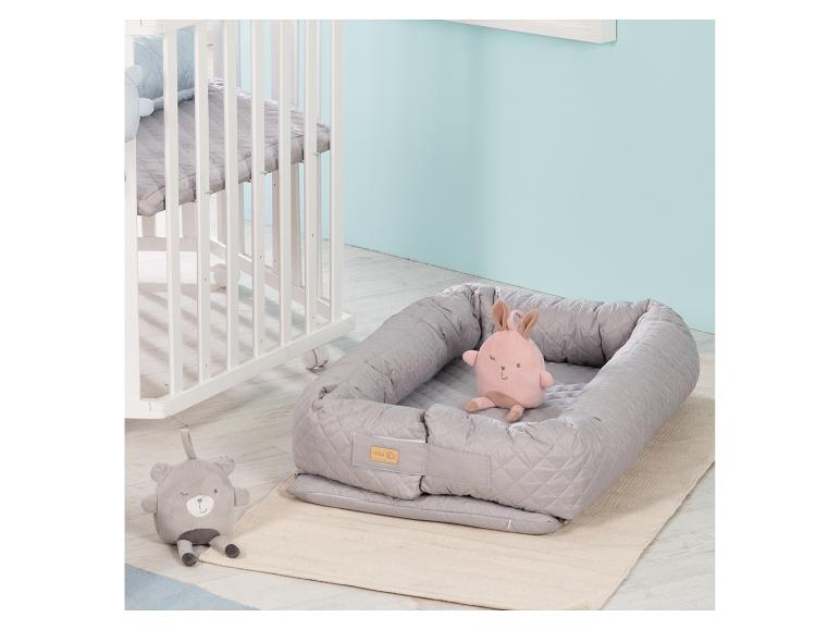 Nid de bébé avec lapin rose et ours en peluche gris à côté d'un berceau blanc