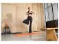 Femme en tenue de yoga noire faisant la posture de l'arbre sur un tapis de yoga orange.