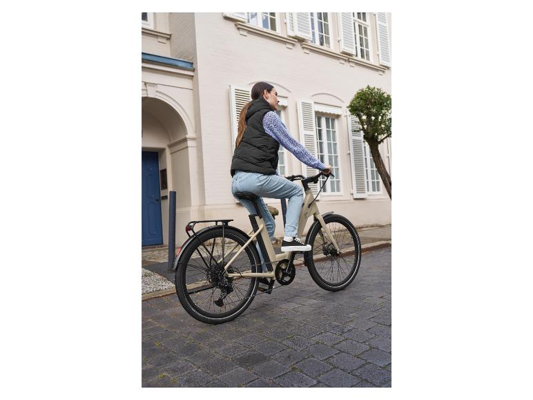 Een vrouw rijdt op een beige elektrische fiets door de stad.
