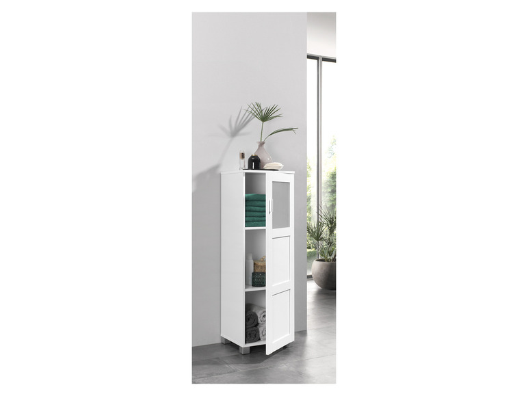 Witte badkamerkast met glazen deur en open vakken, gevuld met handdoeken en decoratie.
