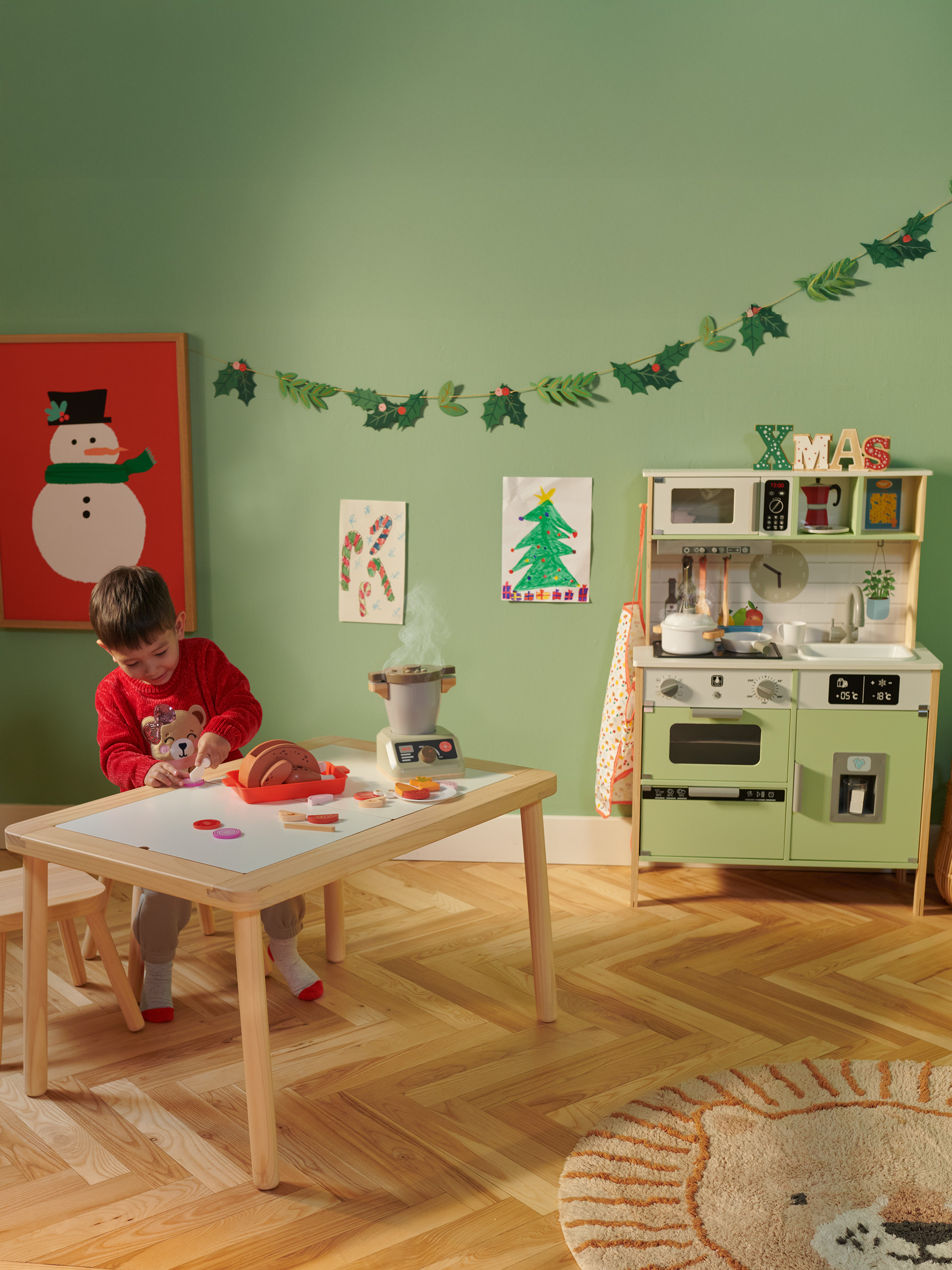 Een kind speelt met een speelkeuken en eettafel in een kerstversierde kamer.