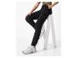 Personne en jogging noir et haut vert, assise sur un tabouret blanc, portant des baskets blanches.
