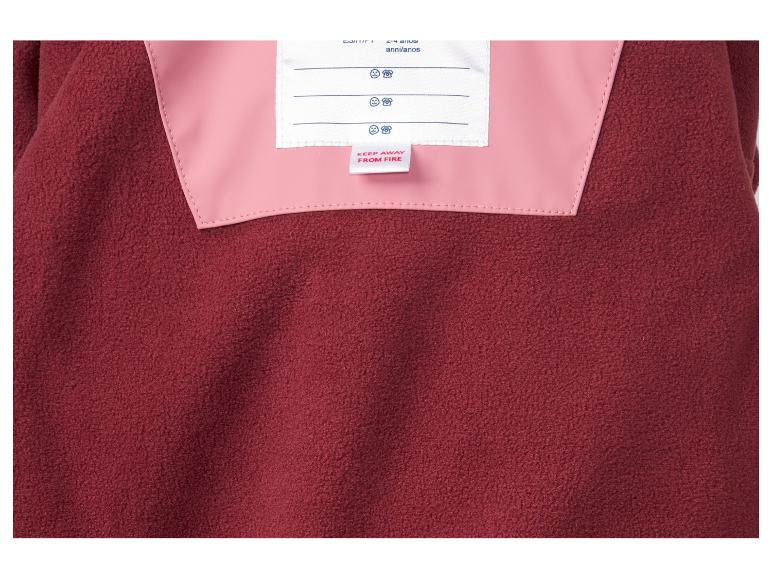 Close-up van een rood fleece kledingstuk met roze binnenvoering en een 'Buiten bereik van vuur houden'-label.