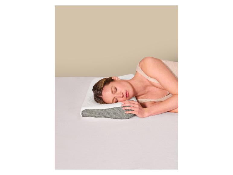 Vrouw slaapt op haar zij op een ergonomisch kussen in een bed met witte lakens.