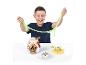Un enfant souriant joue avec de la pâte gluante verte, avec un œuf Dino Fossil Find et des fossiles de dinosaures sur la table.