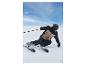 Skieur portant une veste de ski marron et bleu foncé, un pantalon de ski et un casque noir.