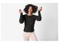 Lachende vrouw in een zwarte top met lange mouwen en lichtroze broek.