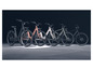 Zwarte, roze, witte en groene elektrische fietsen op een betonnen vloer.
