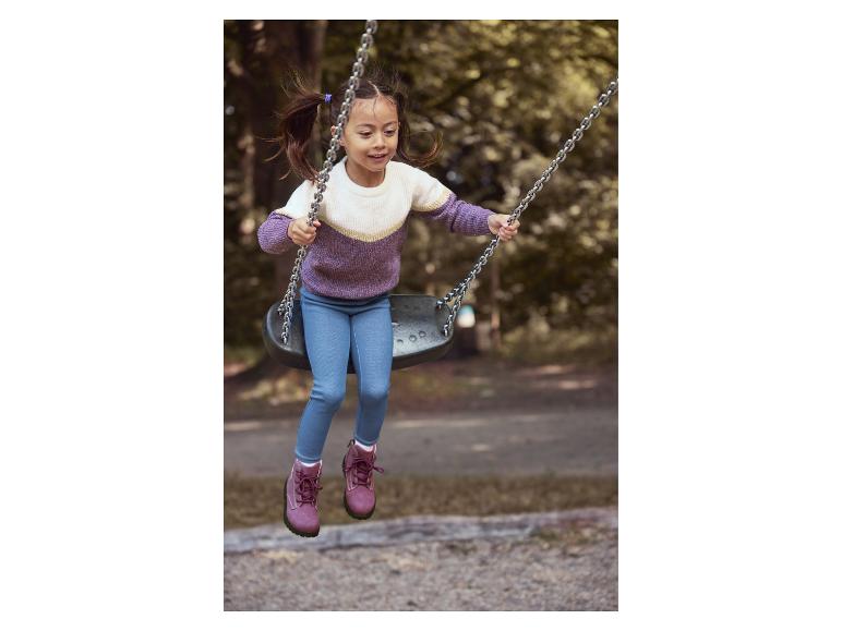 Fille heureuse en pull violet et blanc et jean bleu se balançant dans un parc.