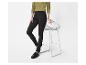 Vrouw in zwarte legging en groene blouse, leunend op een witte barkruk.