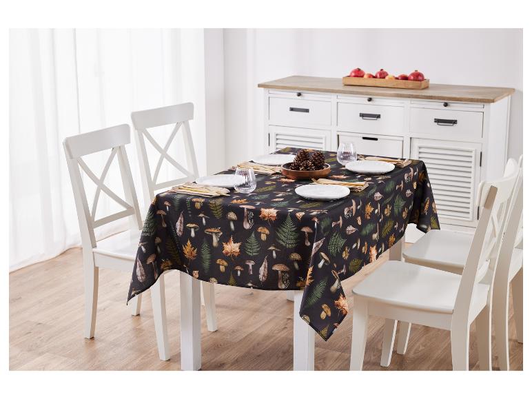 Afbeelding van een tafel met een herfstkleurig tafelkleed met paddenstoelen- en bladerenmotieven en witte stoelen.