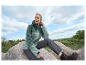 Femme assise sur un rocher, vêtue d'une veste et d'un pantalon de sport.