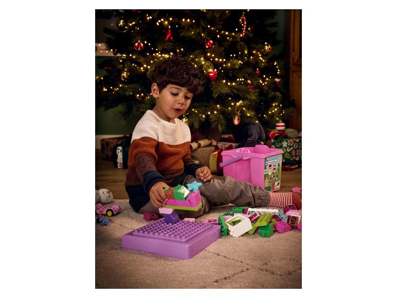 Un enfant joue avec des blocs de construction LEGO DUPLO colorés devant un sapin de Noël.