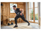 Homme en vêtements de sport noirs utilisant des poids pour une séance d'entraînement dans une maison en bois.