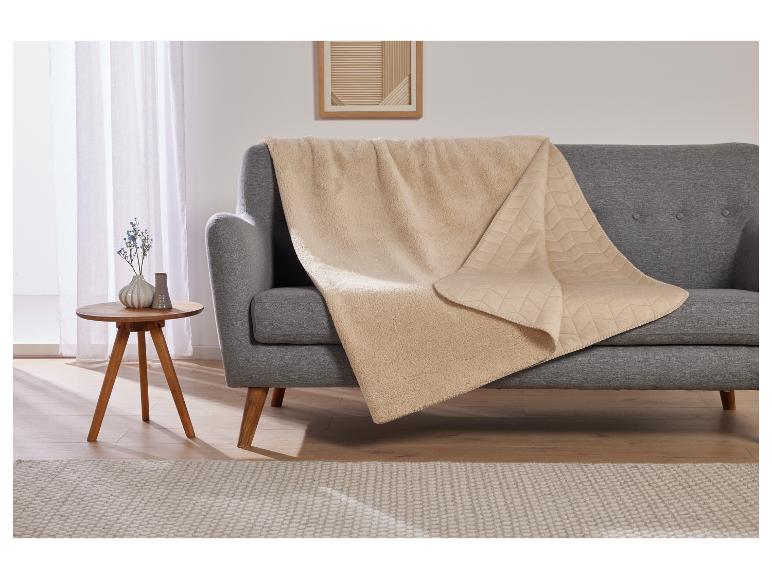 Een beige deken met sherpa-achtige textuur op een grijze bank.