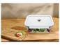 Boîte alimentaire transparente avec couvercle blanc sur une table en bois, avec tomates et mozzarella.