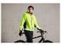 Een man in een felgele fietsjas en zwarte handschoenen staat naast een zwarte fiets.