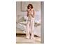 Femme en pyjama rose clair tenant une tasse, debout dans une chambre.