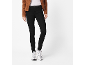 Vrouw met bruine jas, wit T-shirt, zwarte jeans en witte sneakers.