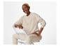 Femme souriante en sweat-shirt et pantalon beige, assise sur une chaise.