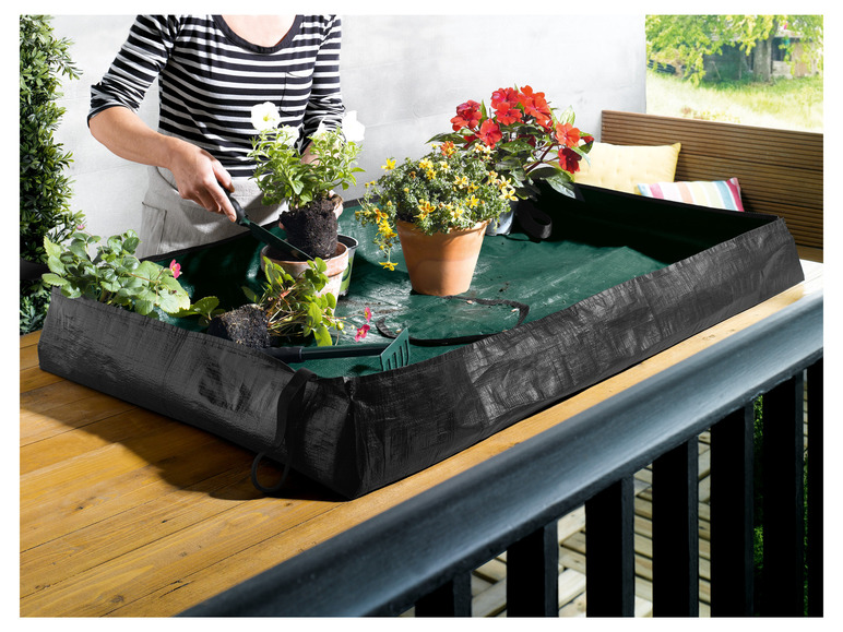 Een zwarte plantenbak op een houten balkon, gevuld met verschillende planten.