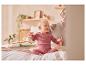 Baby in roze kleding zit op een bed met een volwassene.