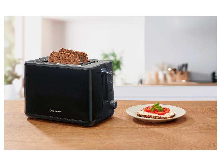 Zwarte broodrooster met twee sneetjes brood en een belegde boterham op een houten tafel.