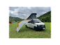 Un van Volkswagen Transporter blanc avec toit relevable et auvent déployé sur un camping.