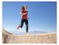 Vrouw rent in rood T-shirt en zwarte legging op stenen muur met bergen.