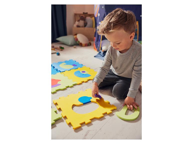 Un petit garçon joue avec des puzzles en mousse de couleur.