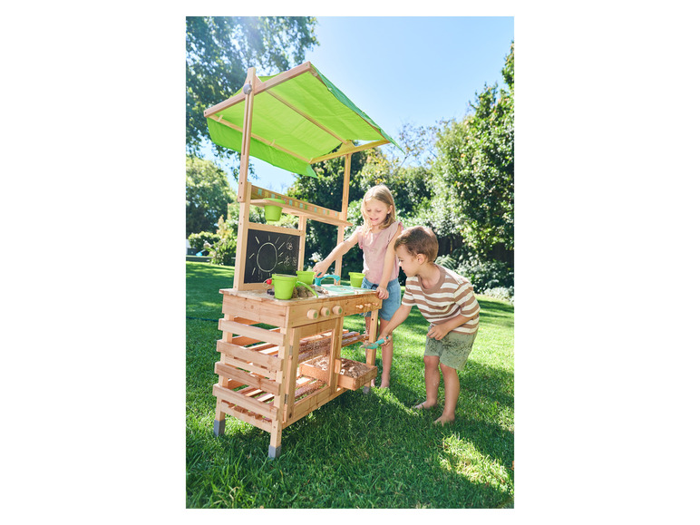 Deux enfants jouent avec une cuisine en bois avec un auvent vert dans le jardin.