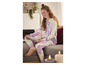 Une femme en pyjama tie-dye assise sur un canapé et regardant une tablette.