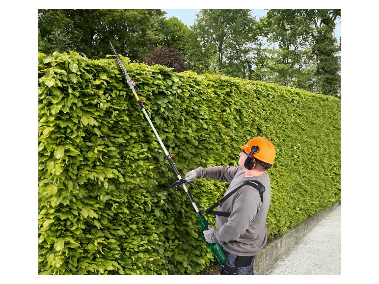 Homme taillant une haie avec un taille-haie sur perche Parkside, portant un casque et des protections auditives.