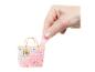 Une main retire une substance rose pailletée d'un mini sac transparent décoré de cœurs et de lettres dorées.