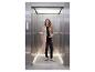 Vrouw in trenchcoat en sneakers in een moderne lift.