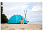 Une femme assise devant une tente bleue sur la plage avec deux pagaies à côté.