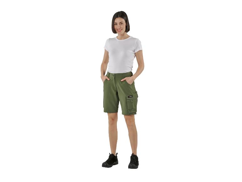 Femme souriante en t-shirt blanc et short cargo vert olive avec des bottes noires.