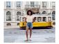 Femme en t-shirt brodé et short en jean devant un tramway jaune en mouvement.