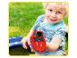Enfant souriant tenant un bateau jouet rouge avec une figurine d'ours dans un jardin vert.