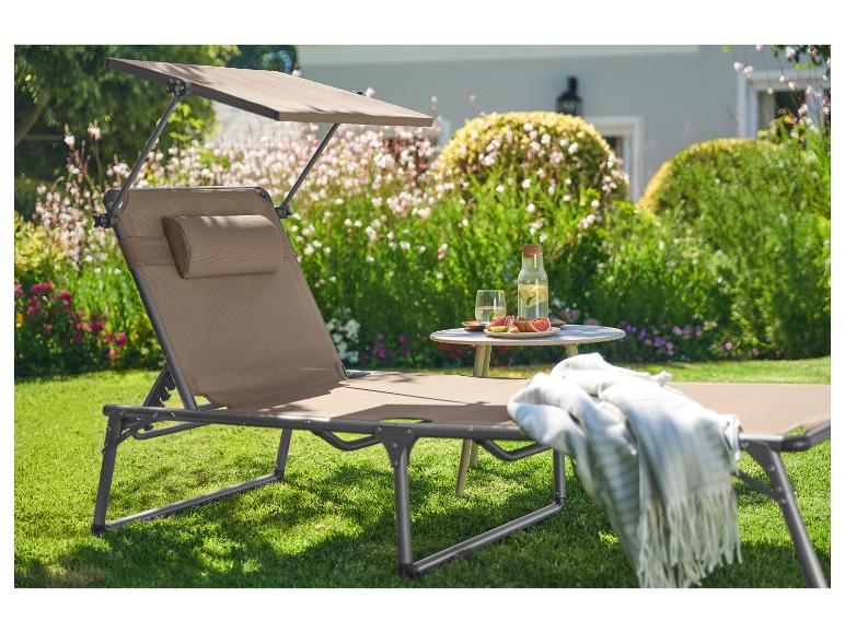 Ligstoel met zonnescherm in een tuin, met drankjes en fruit op een tafel.