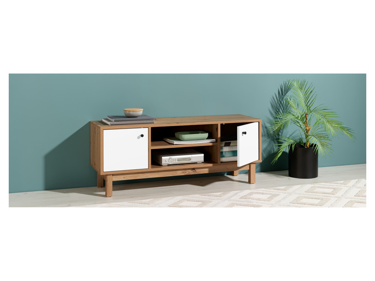 Een houten tv-meubel met witte deuren, een open vak en een plant op de vloer.