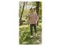 Homme en t-shirt beige et pantalon vert marche dans un parc, chien en arrière-plan.