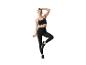 Femme en brassière et legging noirs tenant une corde à sauter, debout sur une jambe.
