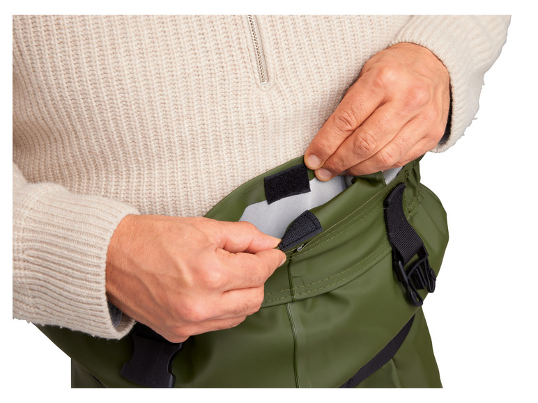 Une personne met un pantalon de pluie vert avec une ceinture noire.