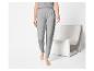 Vrouw in grijs loungewear set, bestaande uit een t-shirt en joggingbroek, staand naast een stoel.