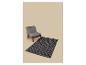 Fauteuil en bois avec coussins gris et tapis noir à motif géométrique.