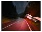 Une main tient une lampe éclairant une route forestière sombre.